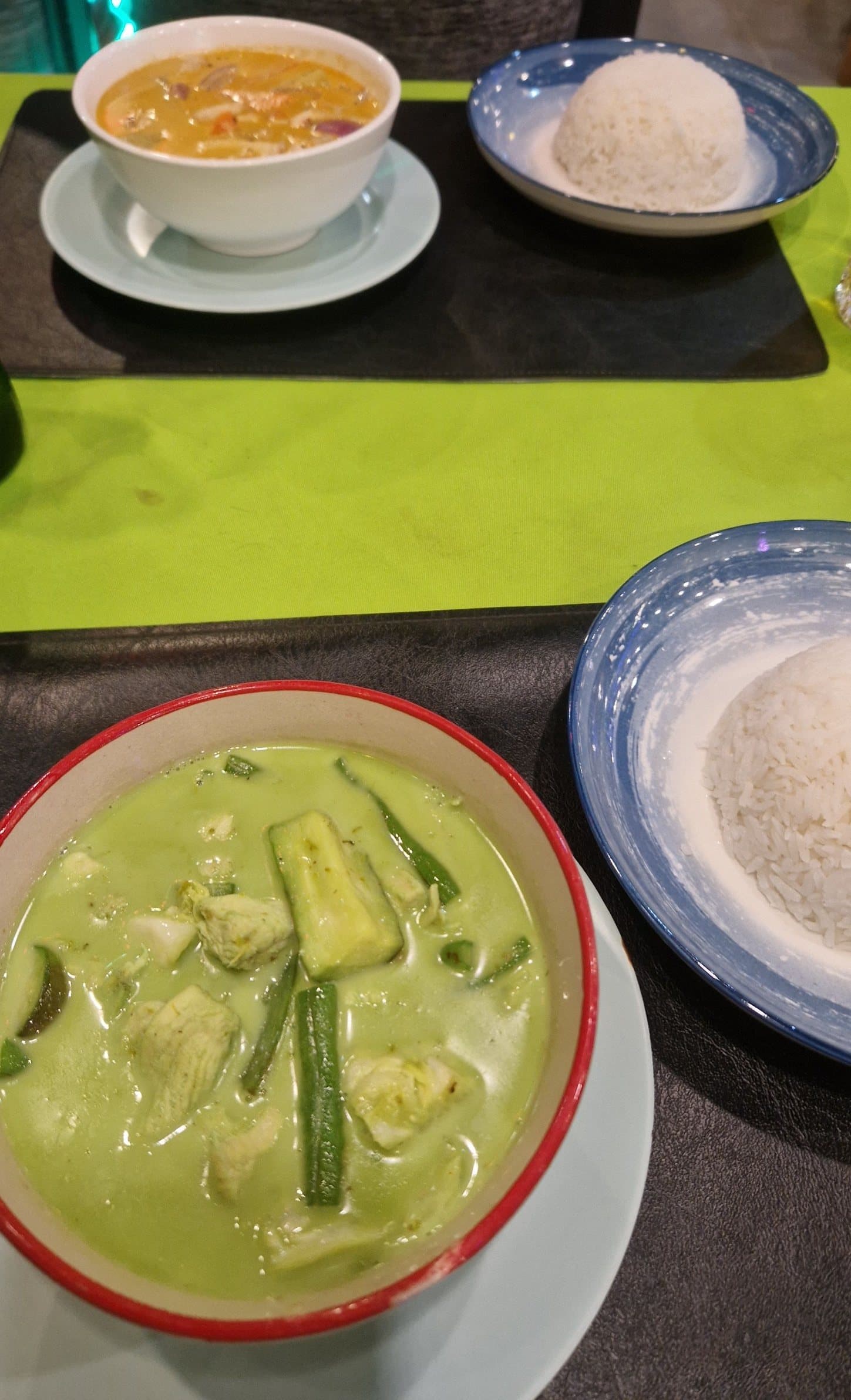 A bowl of red curry and a bowl of green curry, each with a dome of rice, on a table in a Bangkok restaurant