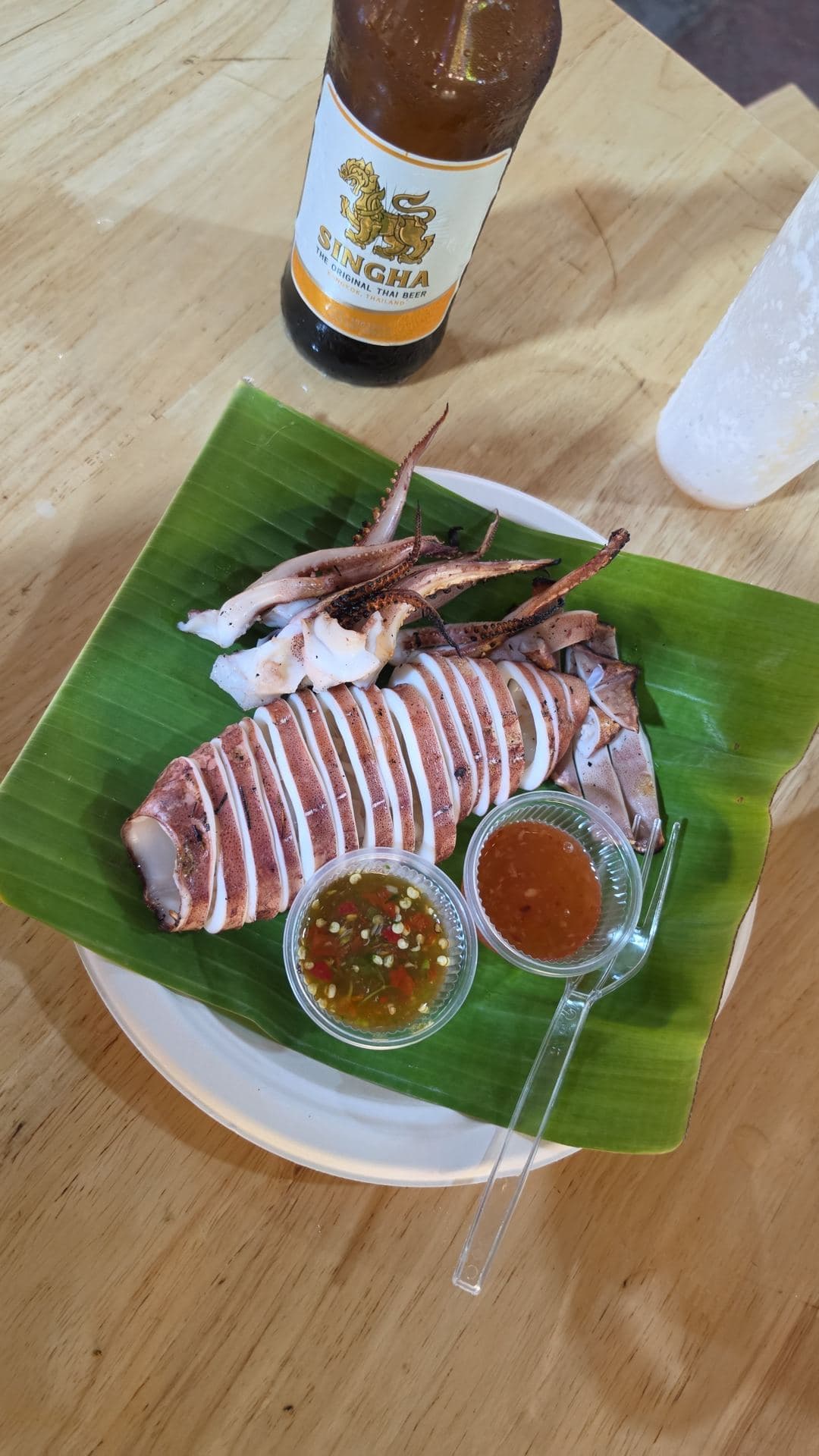Grilled squid on a banana leaf with dipping sauces and a bottle of Singha