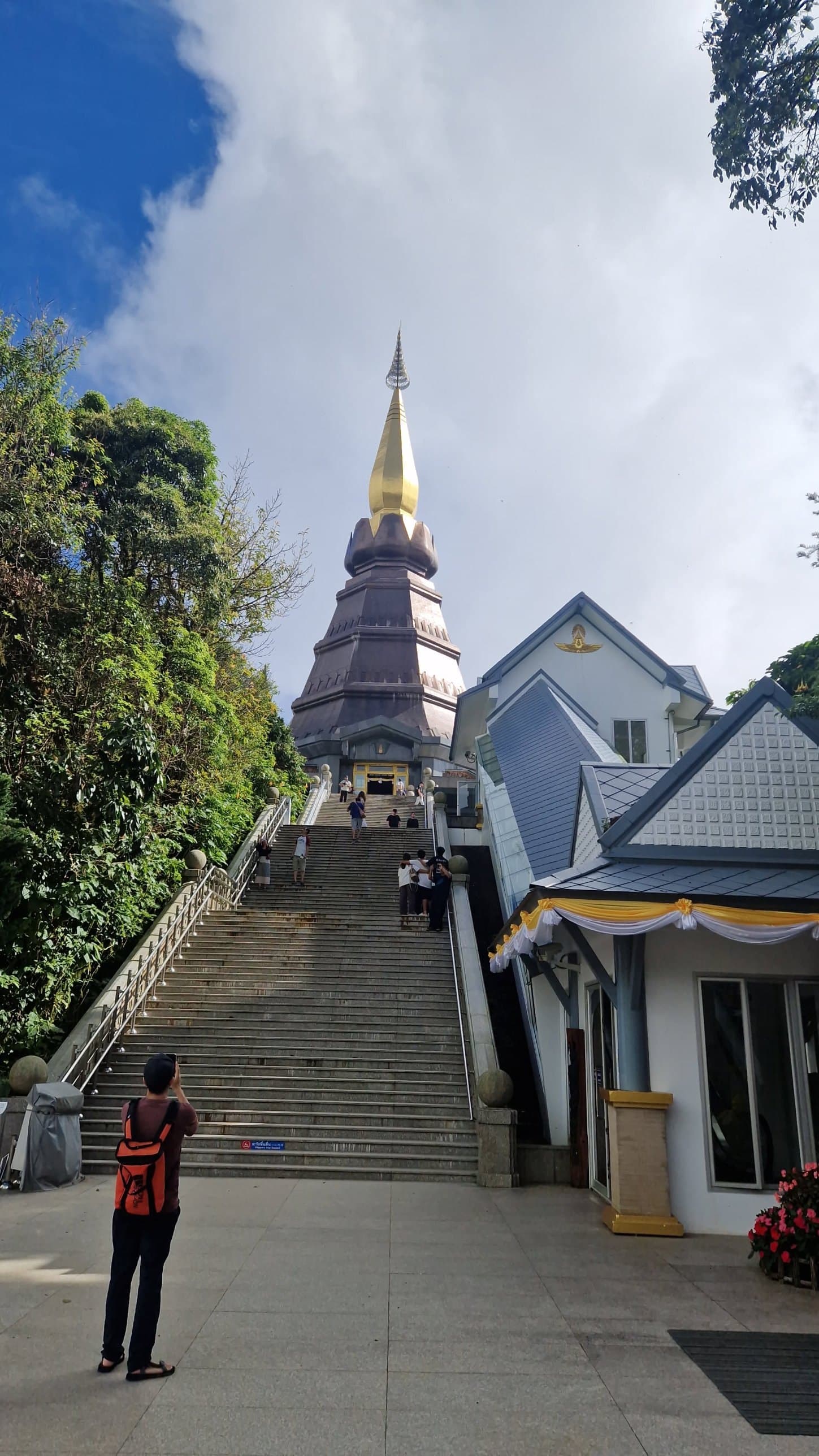 A traveller in an orange backpack on a wide stone staircase leading up to a pagoda