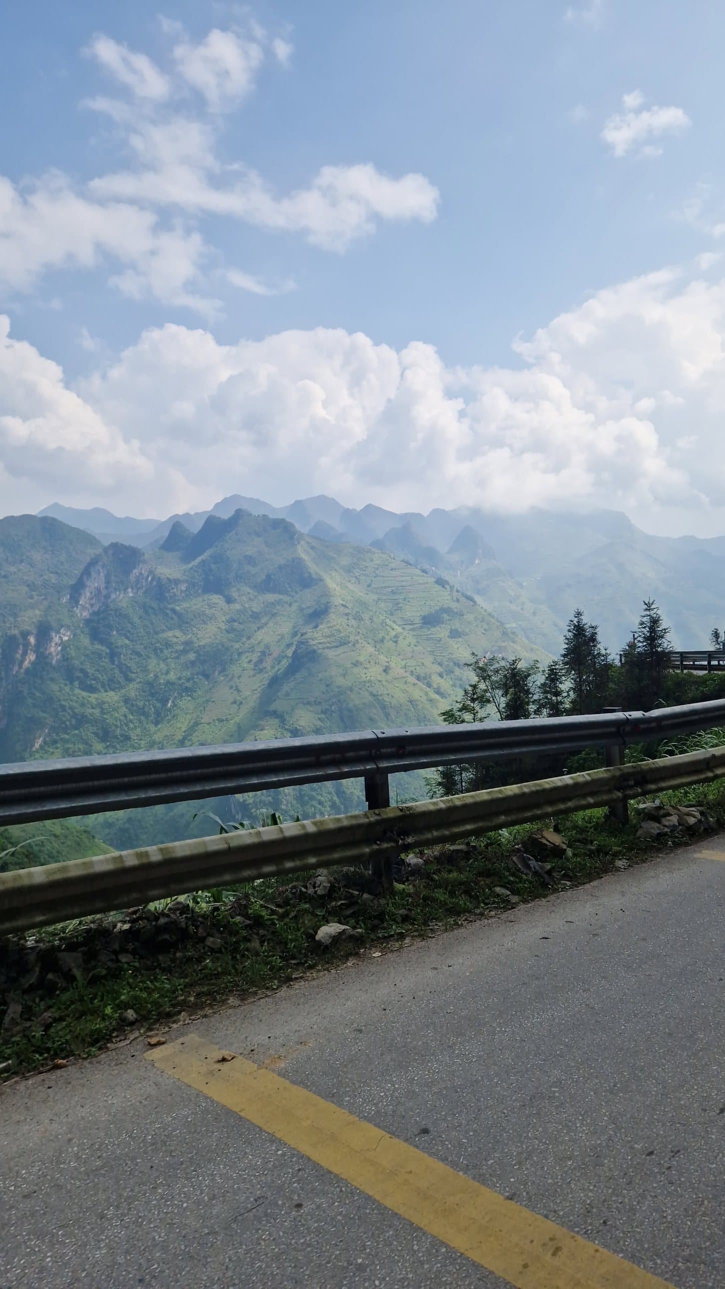 A mountain road with a guardrail, with layered green peaks beyond