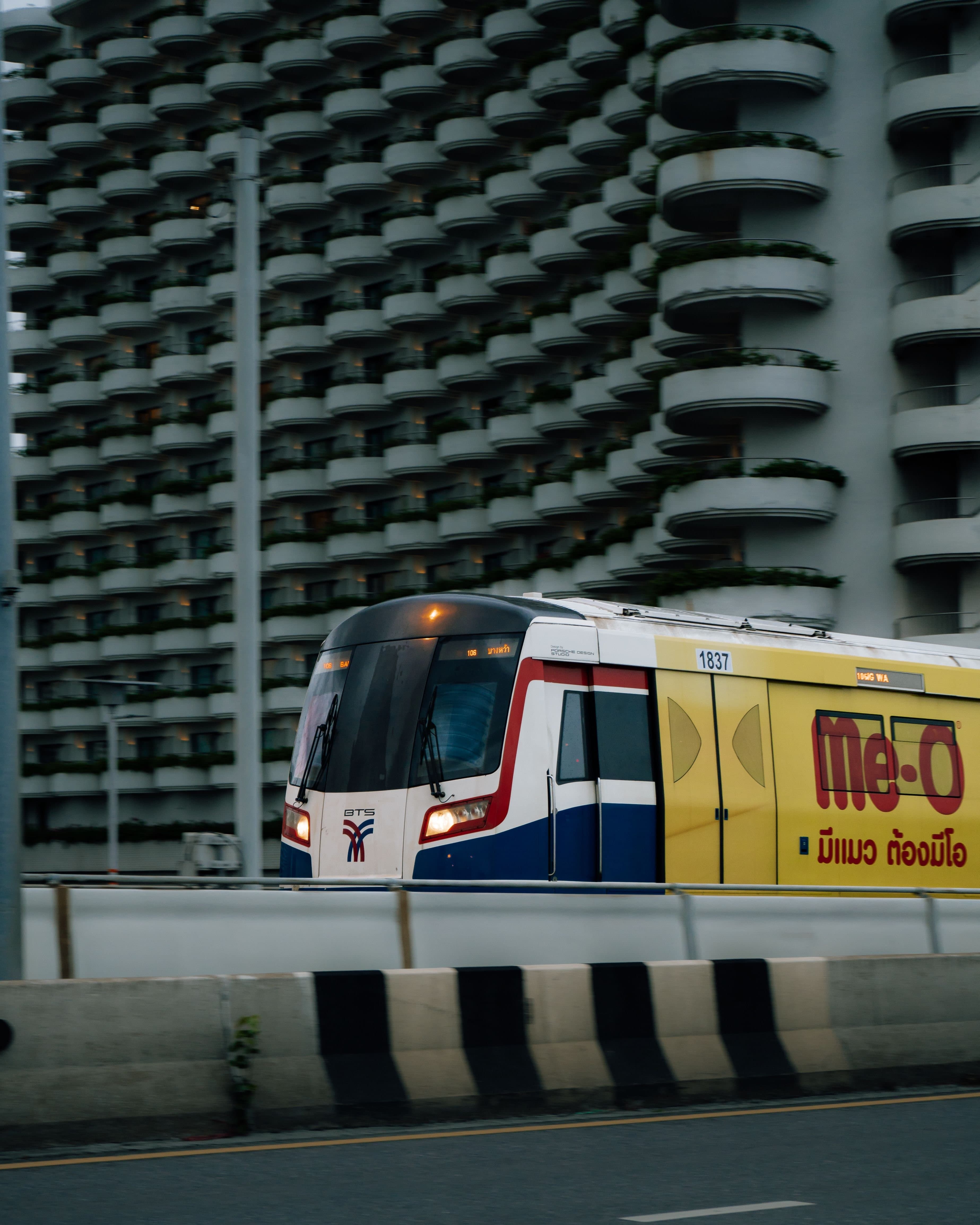 A BTS Skytrain train passing a curved-balcony apartment building in Bangkok