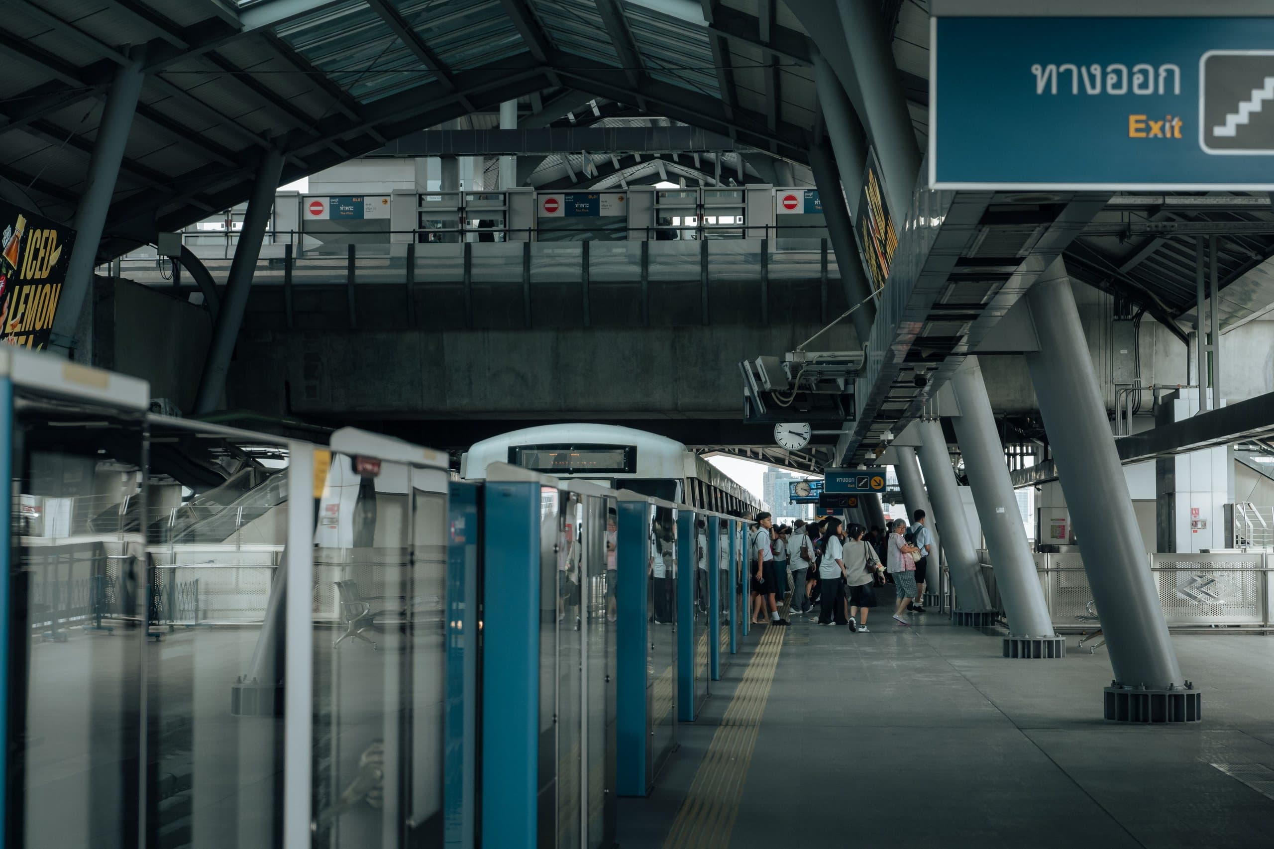 Passengers waiting on an elevated train station platform in Bangkok, behind platform screen doors