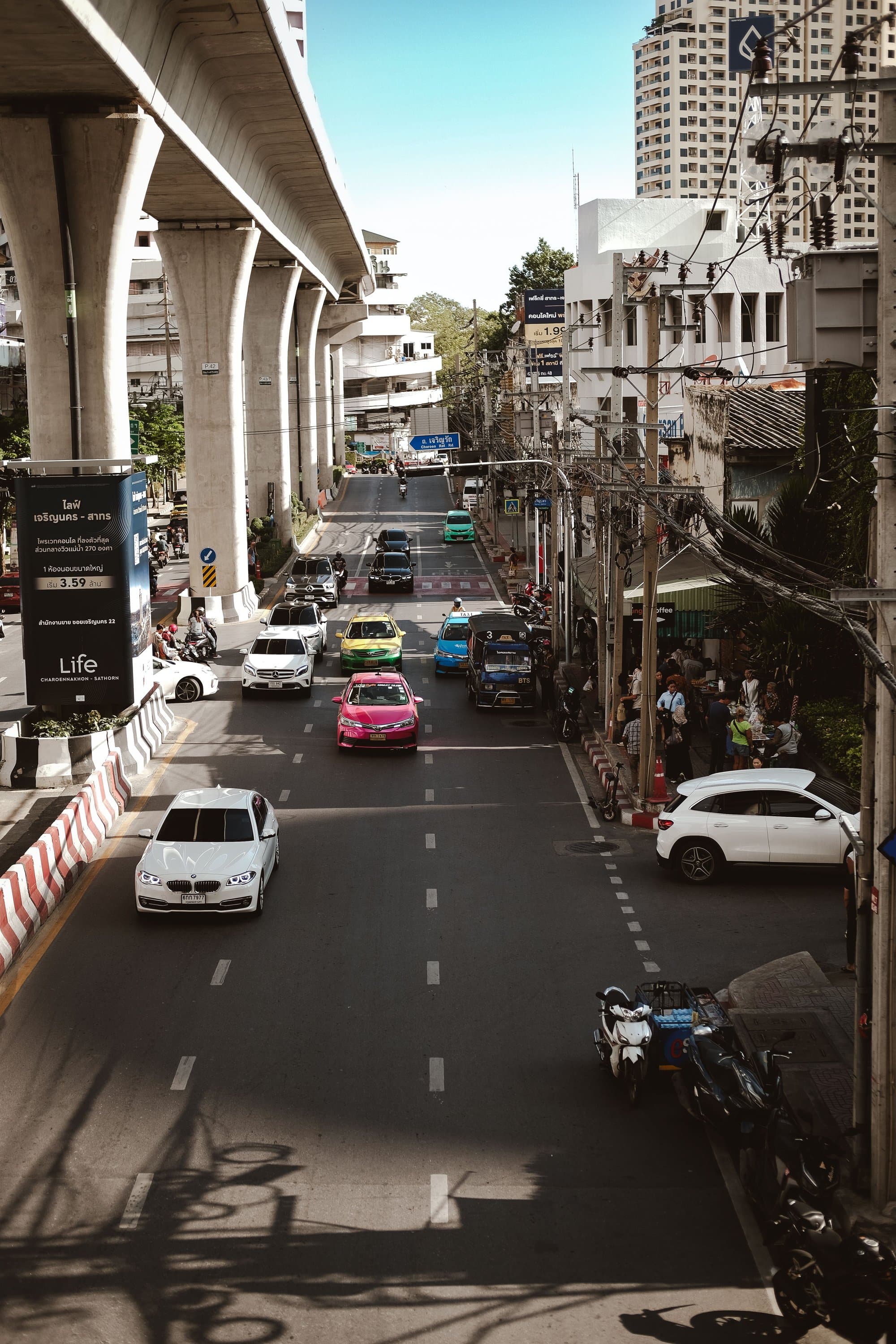 Taxis and traffic on a Bangkok street beneath an elevated railway