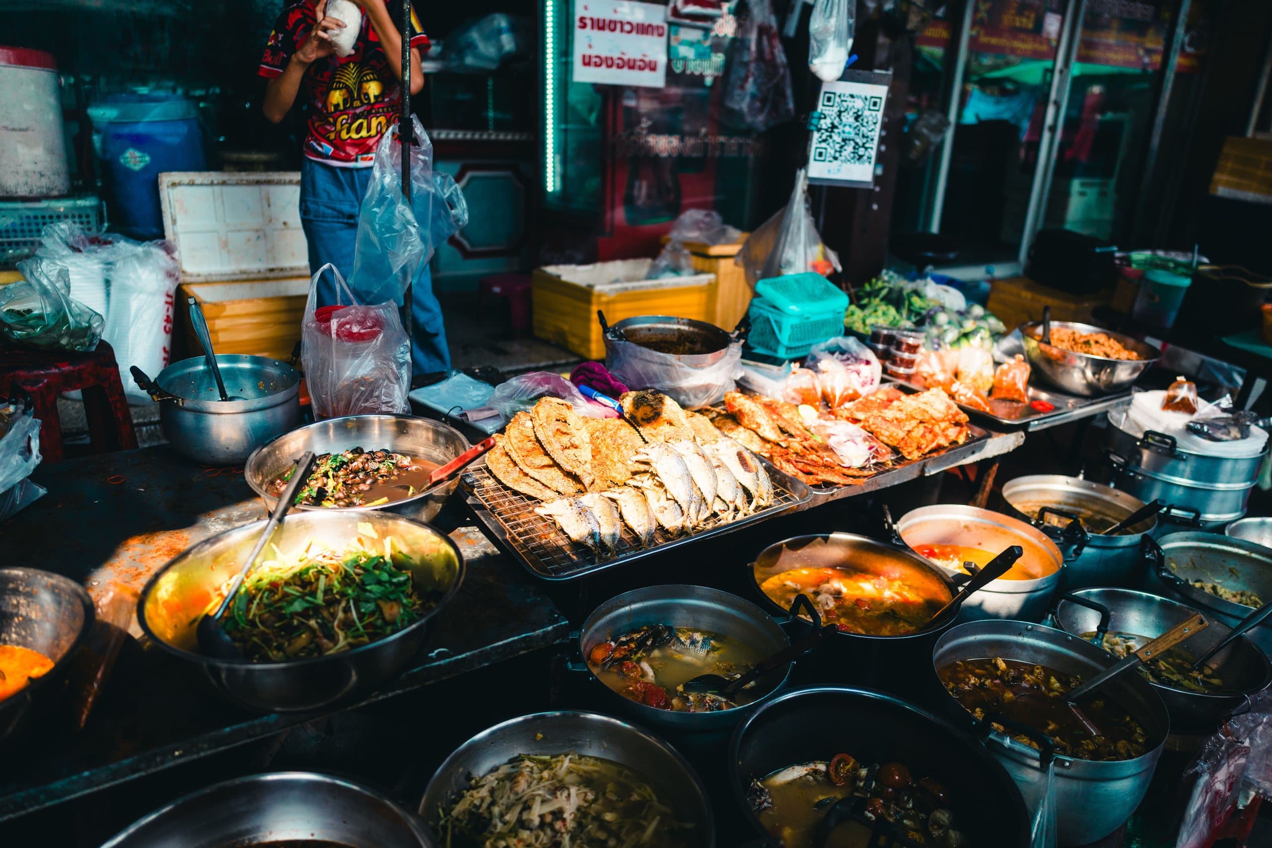 Pots of curries and soups and a tray of fried fish at a street-food stall in Bangkok