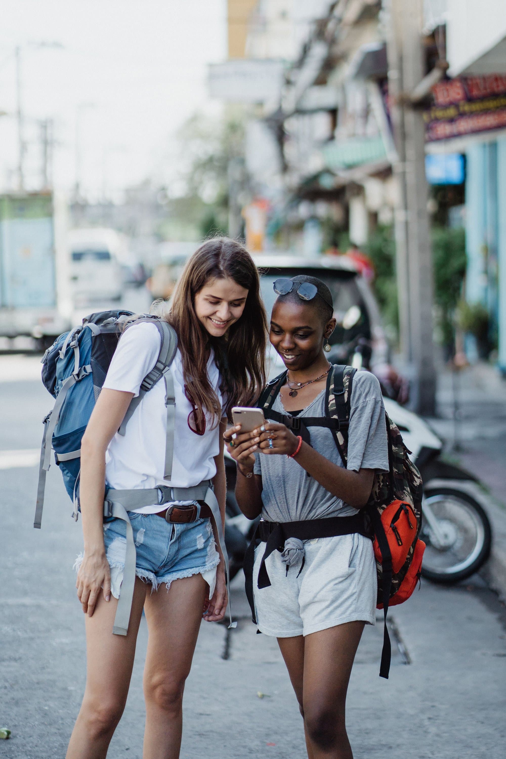 Two travellers with backpacks smiling at a phone on a street in Bangkok