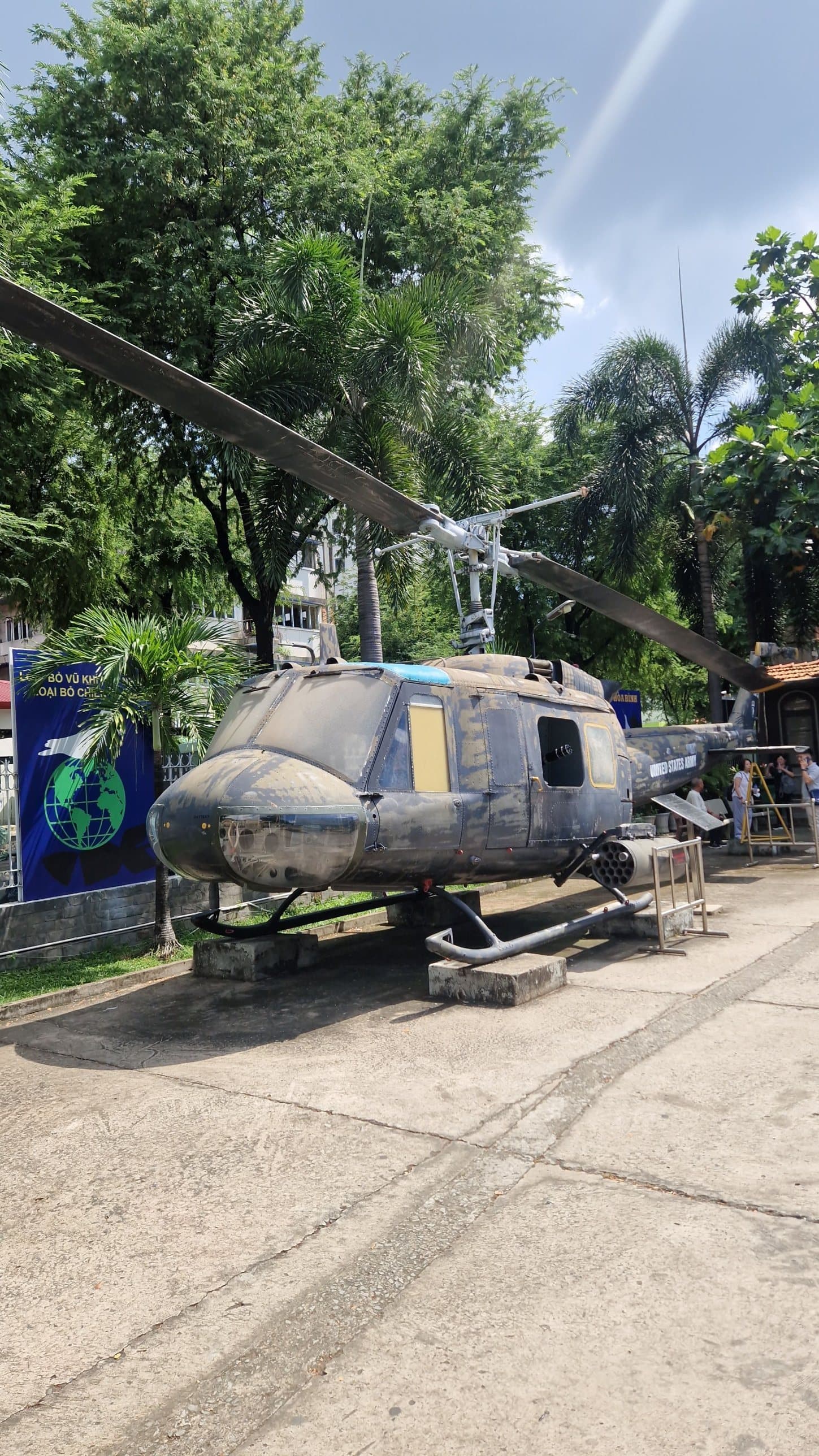 A UH-1 helicopter on display in a museum courtyard, surrounded by trees